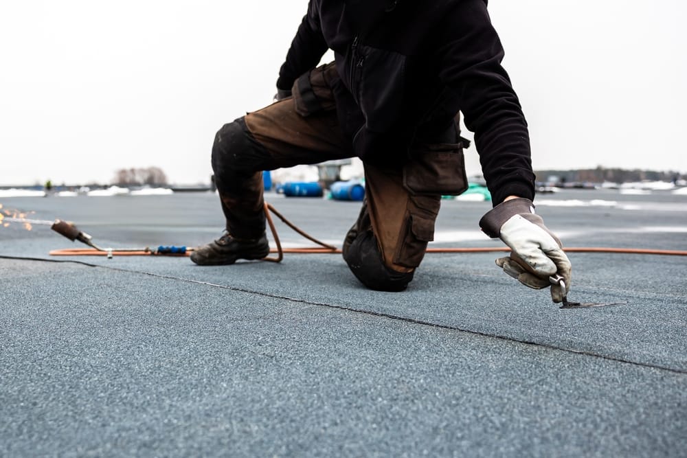 Couvreur professionnel appliquant un rouleau de bitume sur un toit plat à l'aide d'un chalumeau sur un chantier de construction moderne.