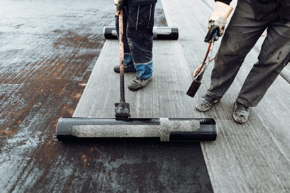 Ouvriers de construction, toitures installant des rouleaux de membrane d'étanchéité bitumineuse