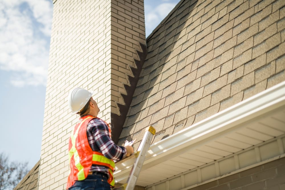 Un homme portant un casque de sécurité se tient sur les marches et inspecte le toit de la maison.