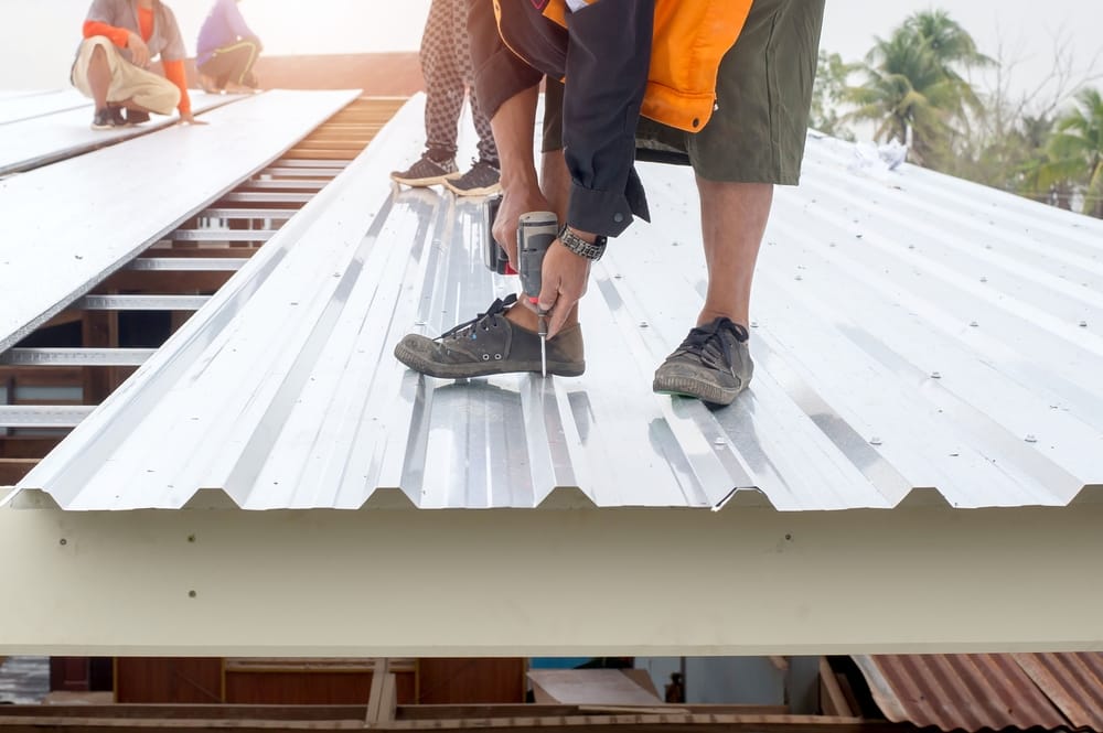 Ouvrier du bâtiment installant un nouveau toit, outils de couverture, perceuse électrique utilisée sur des toitures neuves avec des feuilles de métal.