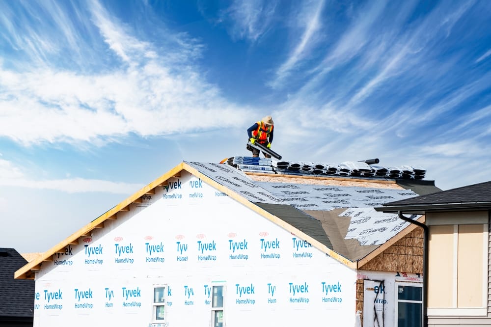 Roofer at work on a new home under construction with shingles and supplies.