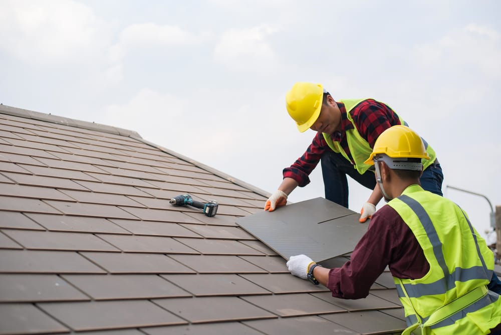Gray roof - Repair and replace the roof of the house with Handyman with tools and protective equipment. Standing on the roof with the sky background Two Asian male roof mechanic
