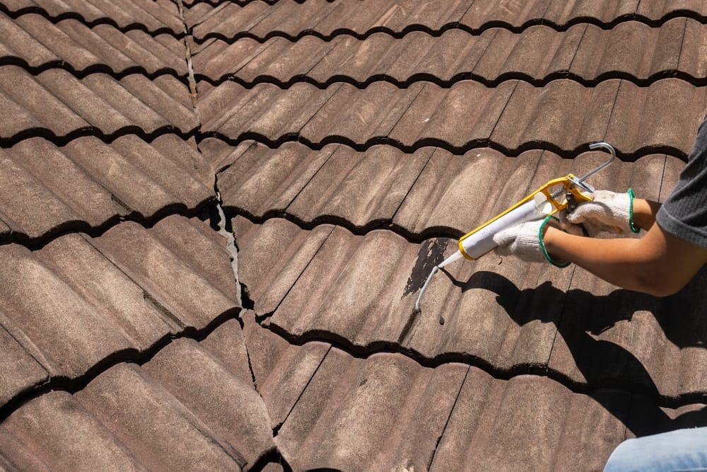 Worker man using silicone sealant adhesive to fix crack of the old tile roof.