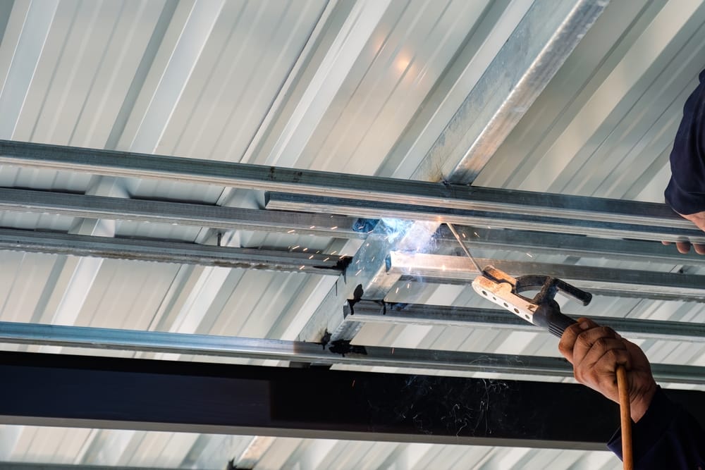 Construction worker installing and welding with flying sparks on steel frame of roof structure in construction site