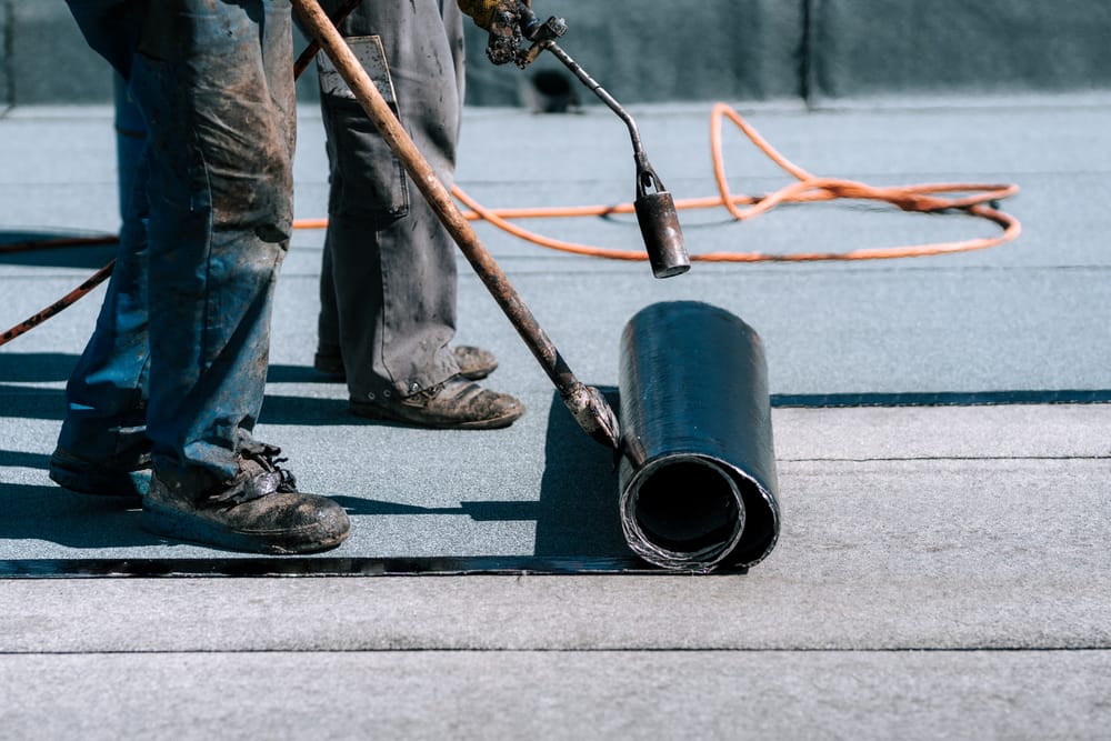 Ouvriers du chantier, toitures installant des rouleaux de membrane d'étanchéité bitumineuse pour l'imperméabilisation de la nouvelle maison
