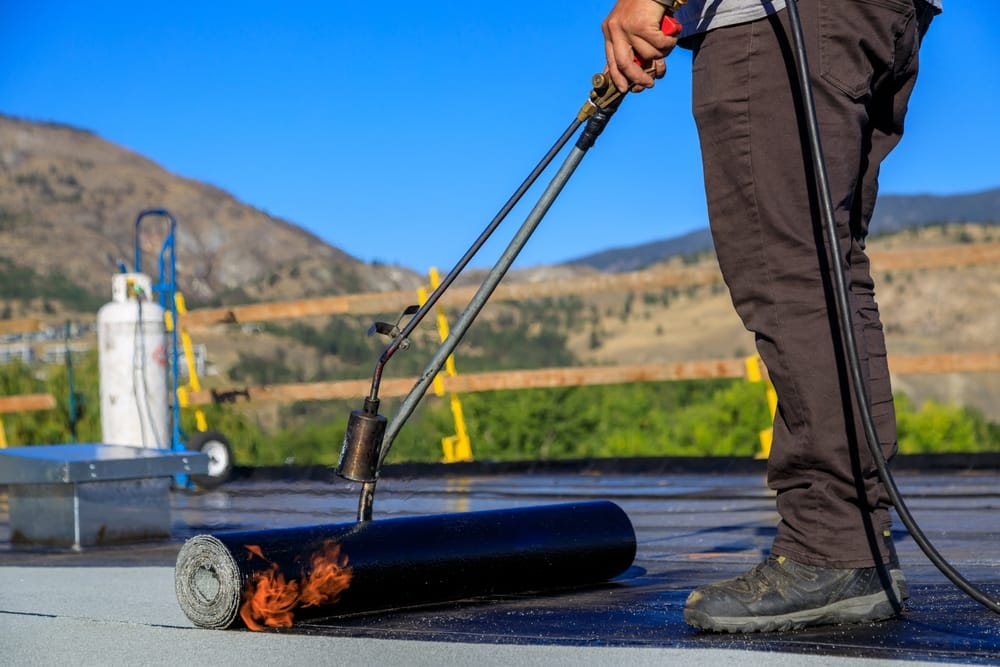 L'invention concerne un couvreur qui applique une couche de membrane sur un toit plat à l'aide d'une torche tigrée pour sceller le bitume asphaltique, assurant ainsi une couche imperméable durable.
